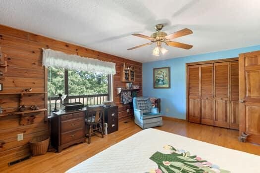 bedroom featuring ceiling fan, light wood-type flooring, wooden walls, and a closet