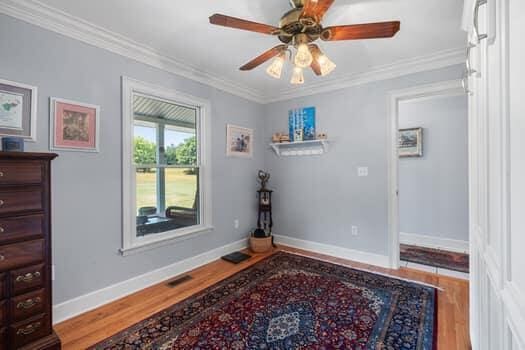 interior space with ceiling fan, wood-type flooring, and ornamental molding