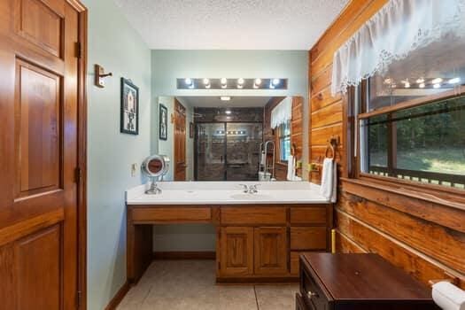 bathroom with walk in shower, vanity, a textured ceiling, tile patterned flooring, and wood walls