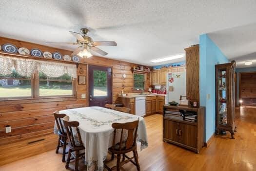 dining room with a textured ceiling, light hardwood / wood-style flooring, ceiling fan, and wooden walls