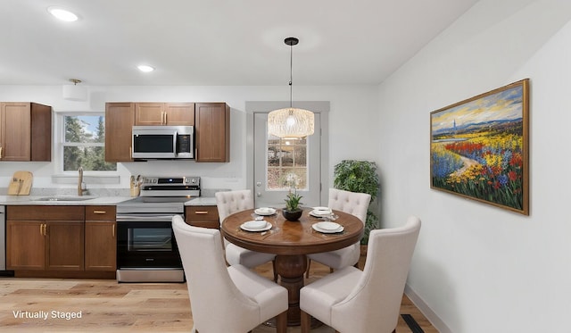 kitchen with appliances with stainless steel finishes, sink, hanging light fixtures, and light hardwood / wood-style flooring