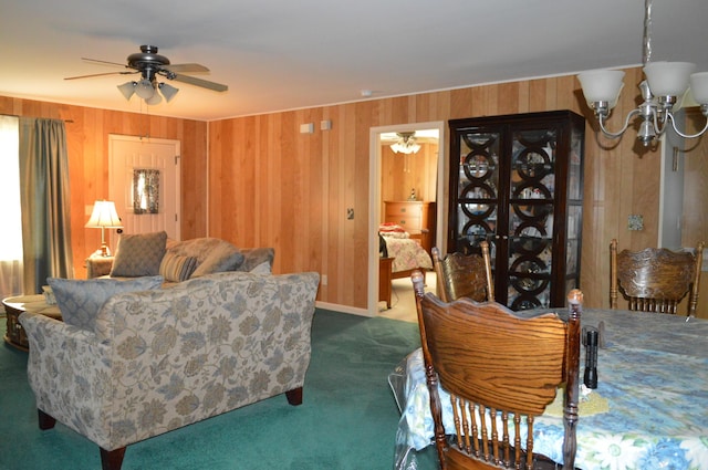 carpeted living room featuring ceiling fan with notable chandelier and wooden walls