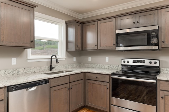 kitchen featuring sink, light wood-type flooring, light stone countertops, ornamental molding, and appliances with stainless steel finishes