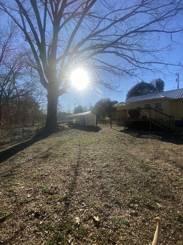 view of yard featuring a storage shed, fence, an outdoor structure, and a wooden deck