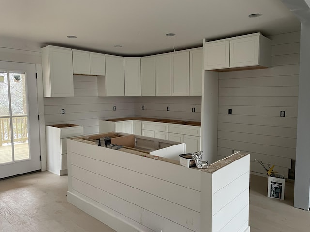 kitchen featuring a kitchen island, light hardwood / wood-style floors, wood walls, and white cabinets