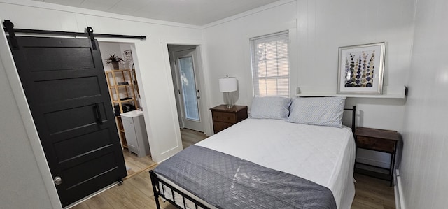 bedroom featuring a barn door, crown molding, and light hardwood / wood-style flooring