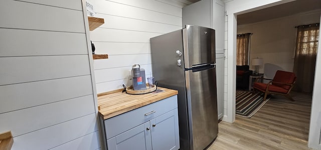 kitchen with wooden walls, light hardwood / wood-style floors, butcher block countertops, and stainless steel refrigerator