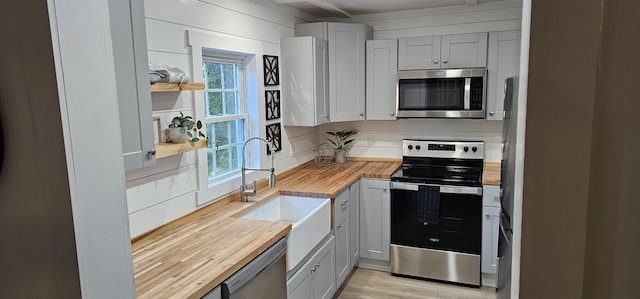 kitchen featuring butcher block counters, wooden walls, sink, and stainless steel appliances