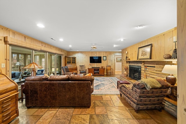 living room with a stone fireplace, ceiling fan, and wood walls