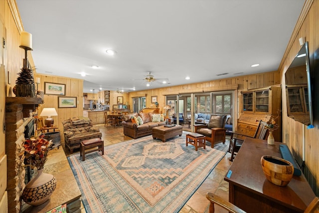 living room featuring ceiling fan, a fireplace, and wood walls