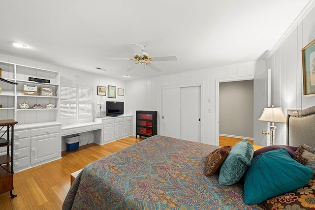 bedroom with built in desk, ceiling fan, and light hardwood / wood-style flooring