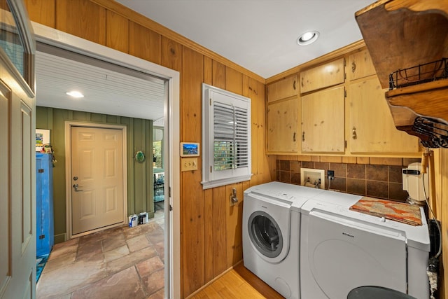 clothes washing area with cabinets, wooden walls, and washing machine and clothes dryer