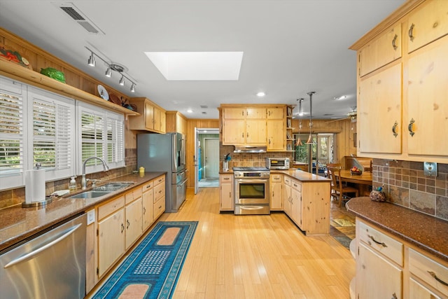 kitchen with sink, appliances with stainless steel finishes, a skylight, light brown cabinetry, and decorative light fixtures