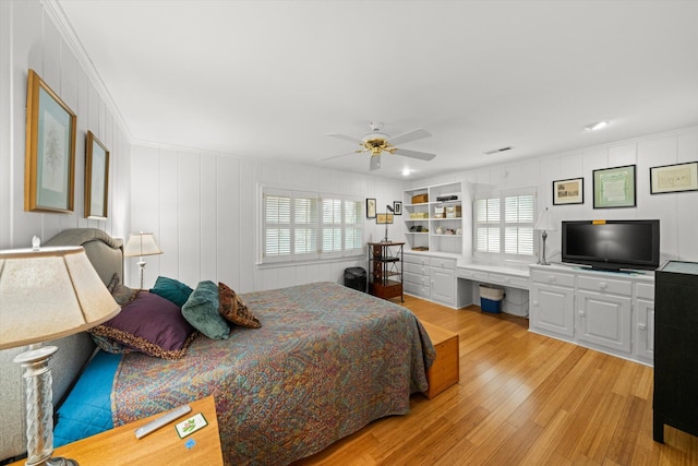 bedroom with ceiling fan, built in desk, multiple windows, and light wood-type flooring