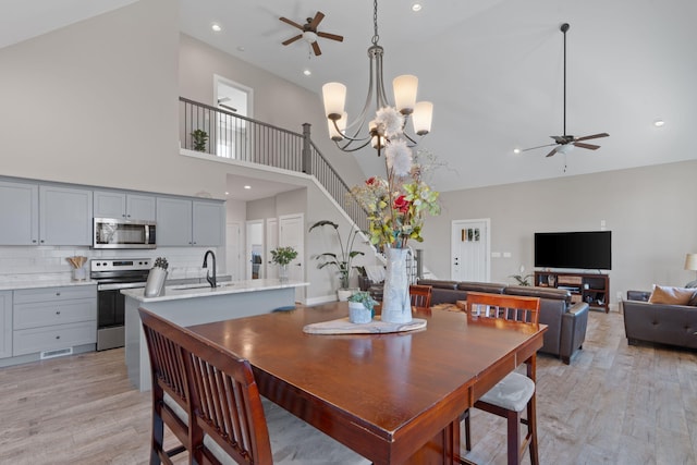 dining area with light wood-style floors, recessed lighting, a high ceiling, and ceiling fan with notable chandelier