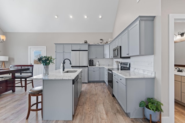 kitchen with appliances with stainless steel finishes, gray cabinets, a sink, and light wood-style flooring