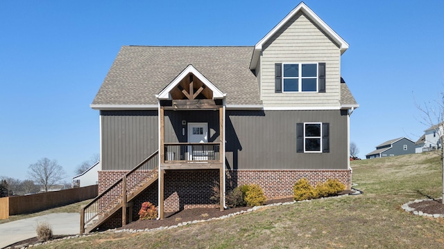 view of front facade featuring roof with shingles, covered porch, stairway, fence, and a front lawn