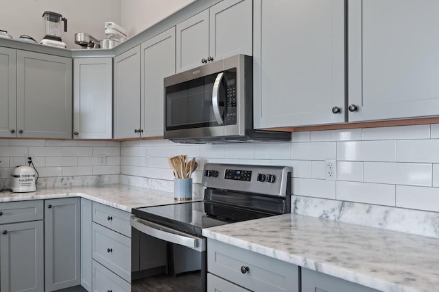 kitchen with stainless steel appliances, tasteful backsplash, light stone countertops, and gray cabinetry