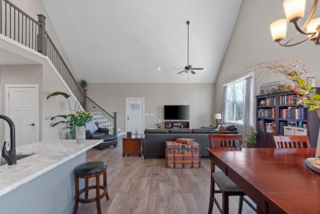 dining space with light wood-style flooring, stairs, high vaulted ceiling, and ceiling fan with notable chandelier