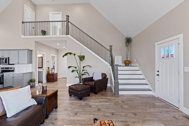 foyer featuring light wood-style flooring, stairs, high vaulted ceiling, and baseboards