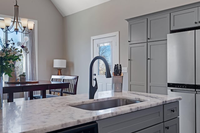 kitchen featuring lofted ceiling, light stone counters, gray cabinetry, a sink, and freestanding refrigerator