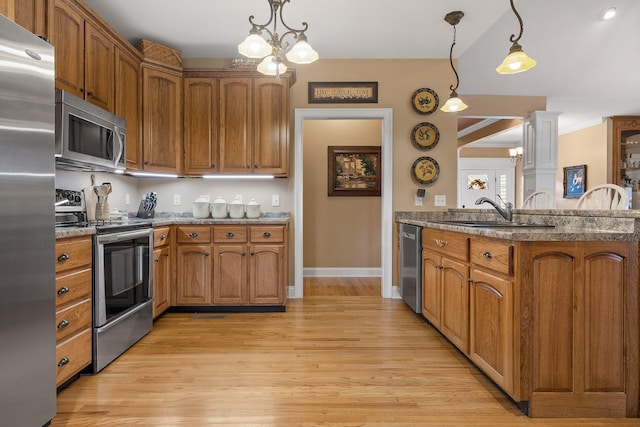 kitchen with sink, light wood-type flooring, stainless steel appliances, and hanging light fixtures