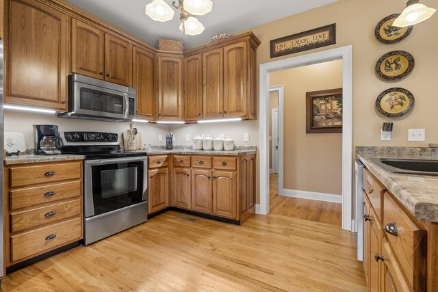 kitchen with appliances with stainless steel finishes, light hardwood / wood-style flooring, pendant lighting, and sink