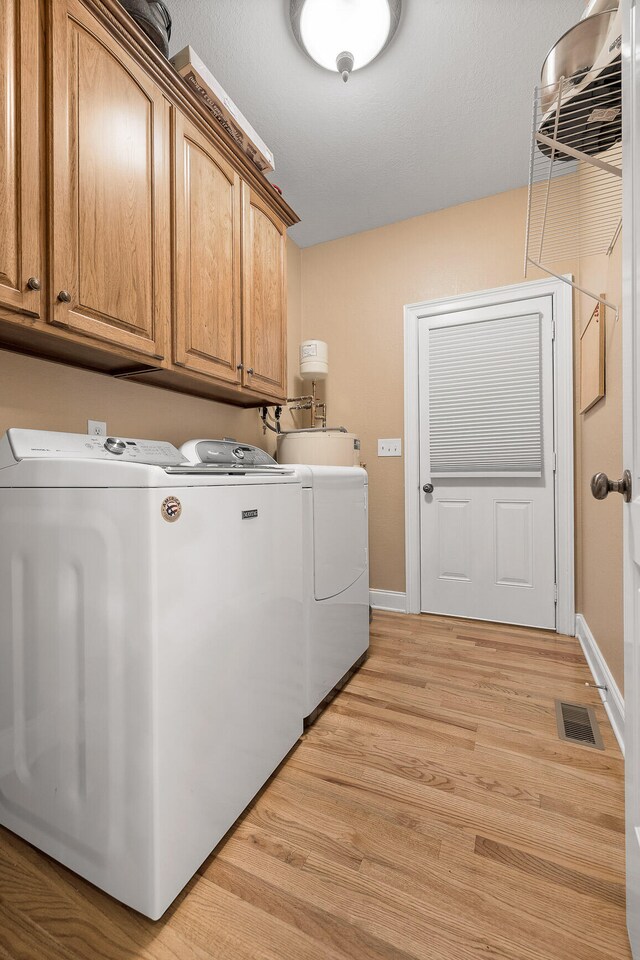 laundry area with light hardwood / wood-style floors, cabinets, and washing machine and clothes dryer