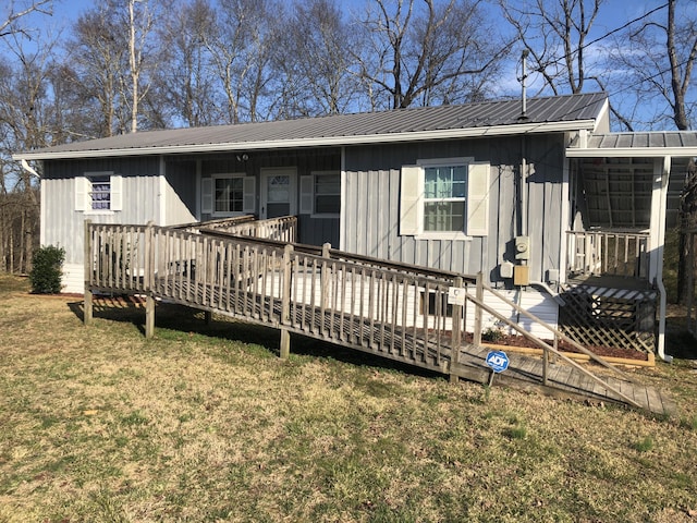 rear view of property with metal roof, a lawn, a wooden deck, and board and batten siding