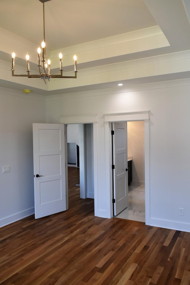 unfurnished bedroom featuring baseboards, a tray ceiling, a chandelier, and dark wood-type flooring