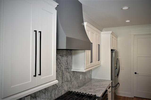 kitchen featuring wall chimney exhaust hood, stainless steel refrigerator with ice dispenser, white cabinetry, and light stone countertops