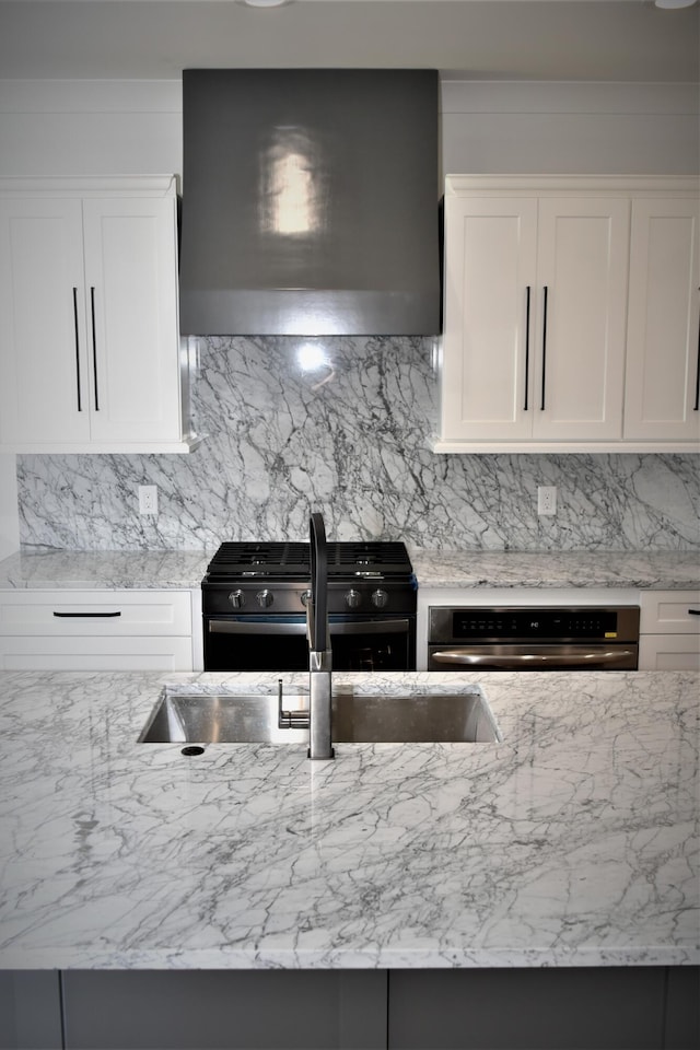 kitchen featuring light stone countertops, oven, wall chimney range hood, and gas range