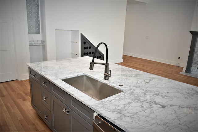 kitchen featuring baseboards, light stone counters, a sink, and wood finished floors