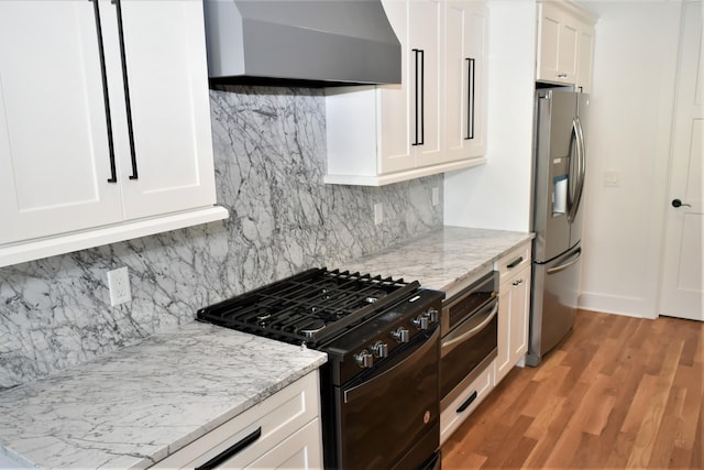 kitchen with light stone counters, black gas range, light wood-style floors, wall chimney range hood, and stainless steel fridge with ice dispenser