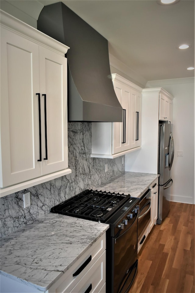 kitchen featuring black range with gas cooktop, stainless steel fridge, decorative backsplash, extractor fan, and white cabinetry