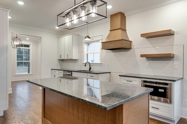 kitchen featuring appliances with stainless steel finishes, custom exhaust hood, sink, white cabinets, and a kitchen island