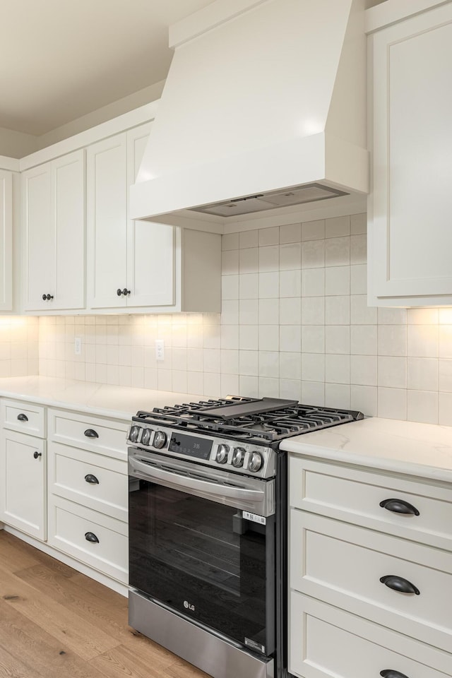 kitchen featuring white cabinetry, stainless steel range with gas cooktop, decorative backsplash, custom range hood, and light wood-type flooring