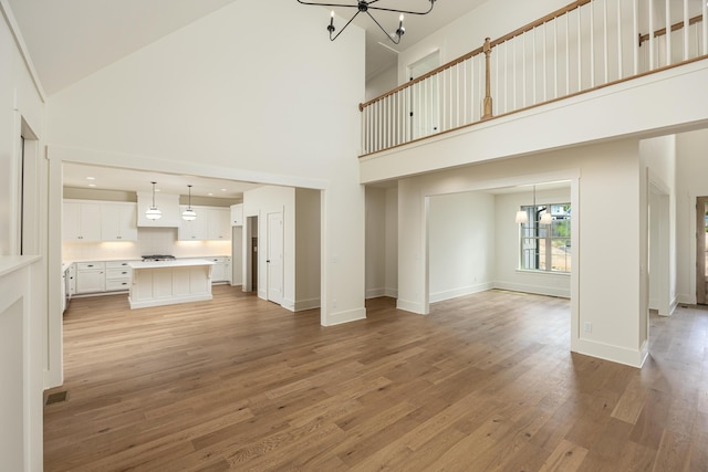 unfurnished living room with light wood-type flooring, high vaulted ceiling, and a chandelier