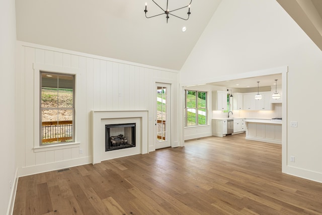 unfurnished living room featuring hardwood / wood-style floors, high vaulted ceiling, a healthy amount of sunlight, and a notable chandelier