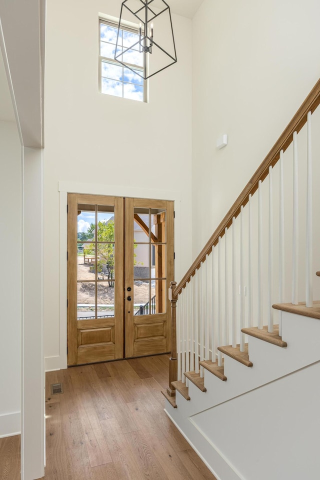 entrance foyer with a chandelier, light hardwood / wood-style flooring, a high ceiling, and french doors