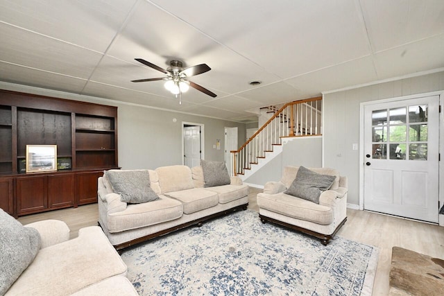 living area with light wood-type flooring, stairs, and ceiling fan