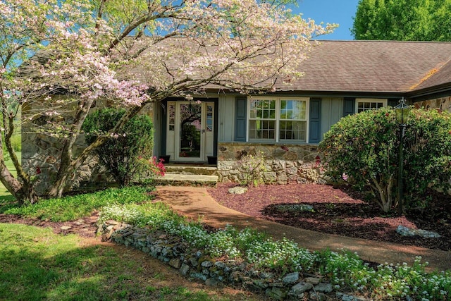 entrance to property with roof with shingles, board and batten siding, and stone siding