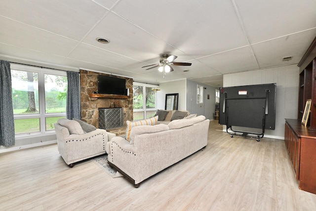 living room with ceiling fan, a stone fireplace, light wood-style flooring, and visible vents