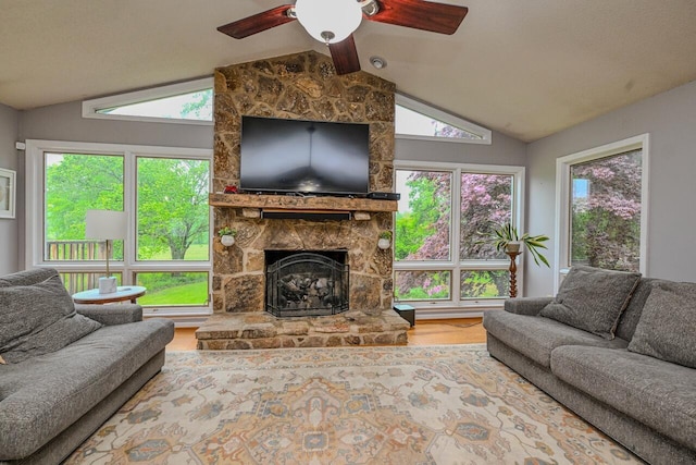 living room featuring a stone fireplace, a ceiling fan, wood finished floors, and lofted ceiling