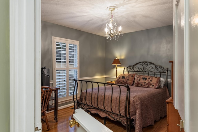 bedroom with a textured ceiling, hardwood / wood-style flooring, and an inviting chandelier