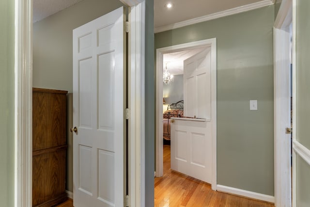 hallway with a textured ceiling, light wood-type flooring, ornamental molding, and an inviting chandelier