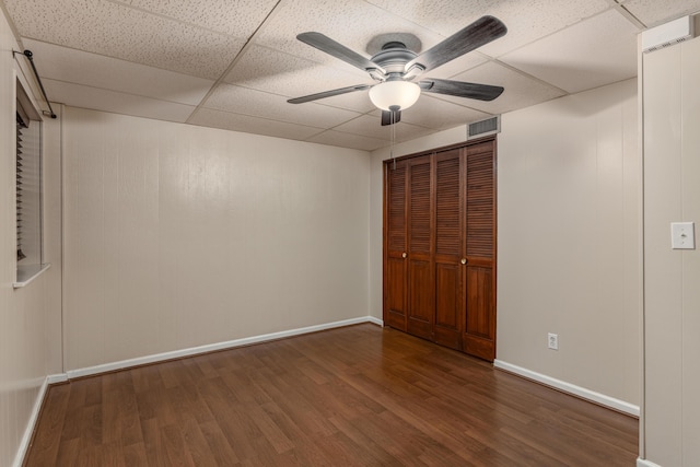 unfurnished bedroom with a drop ceiling, dark wood-type flooring, and ceiling fan