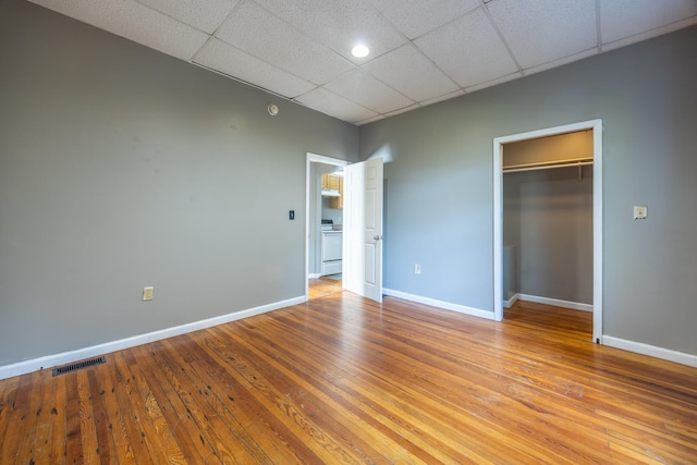 unfurnished bedroom with a walk in closet, a closet, a drop ceiling, and light wood-type flooring