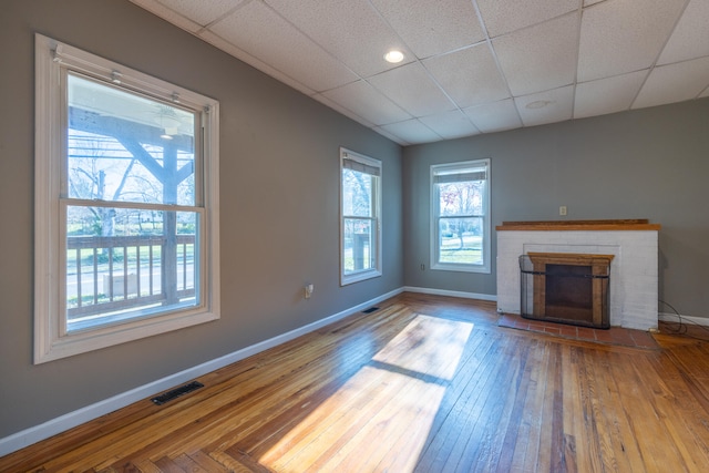 unfurnished living room featuring a fireplace, hardwood / wood-style flooring, and a drop ceiling