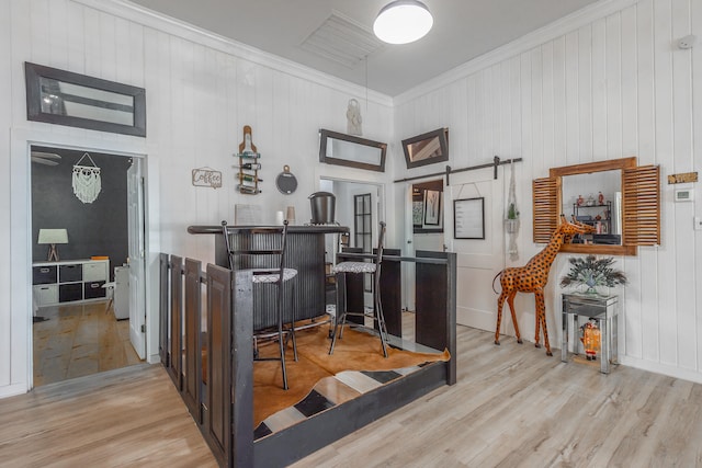 bar with wooden walls, a barn door, light hardwood / wood-style floors, and crown molding